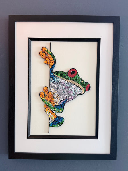 Picture of a frog in a black frame with a white mount, on a blue background